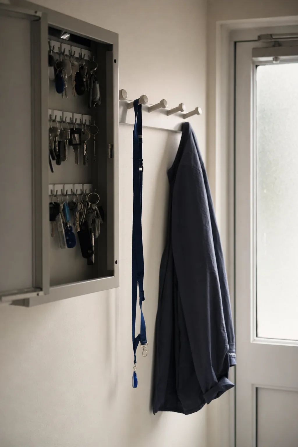 A key cabinet and coat pegs by the back door of a small clinic, one lanyard hanging.