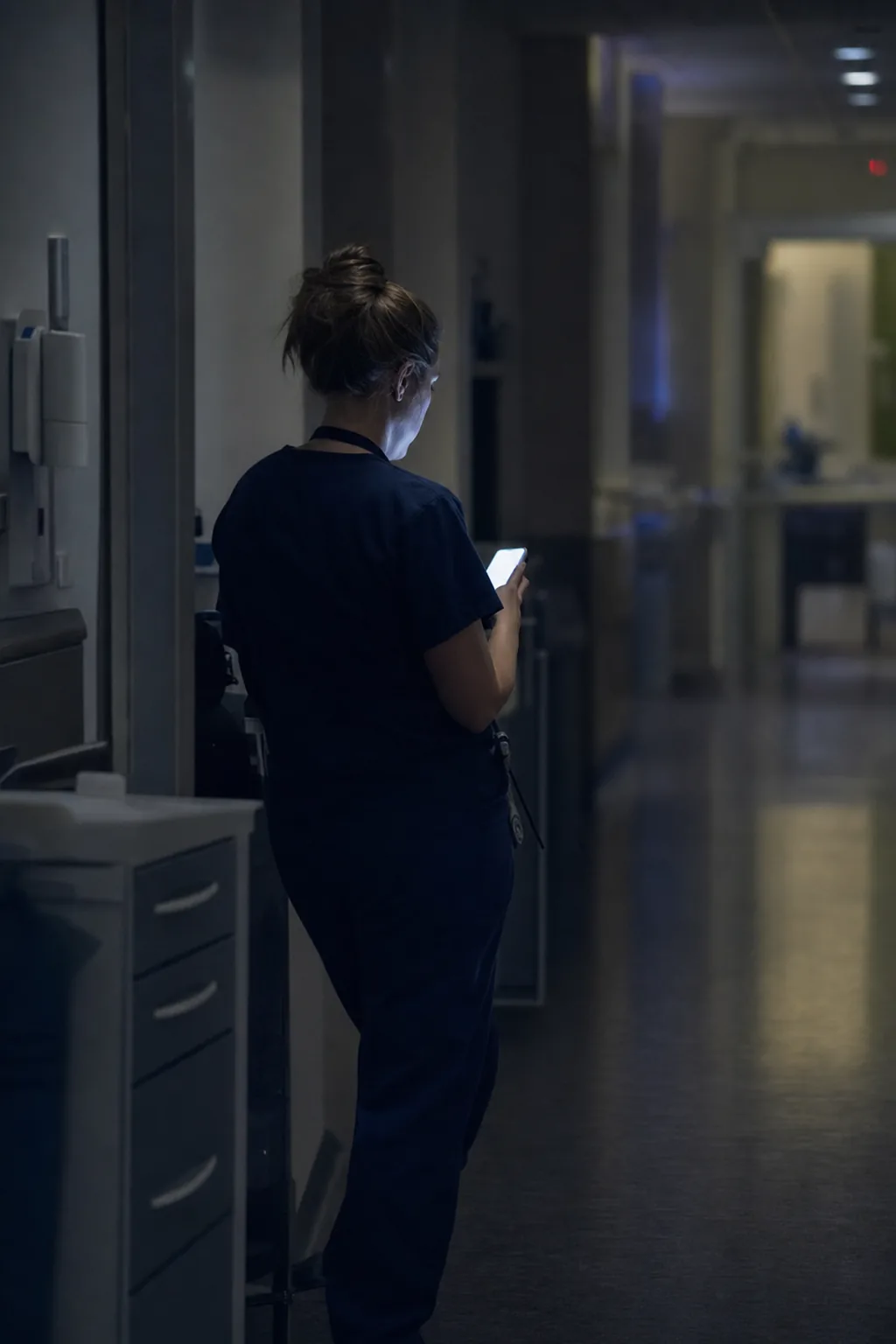 A nurse checking her phone in a dim hospital corridor at night.