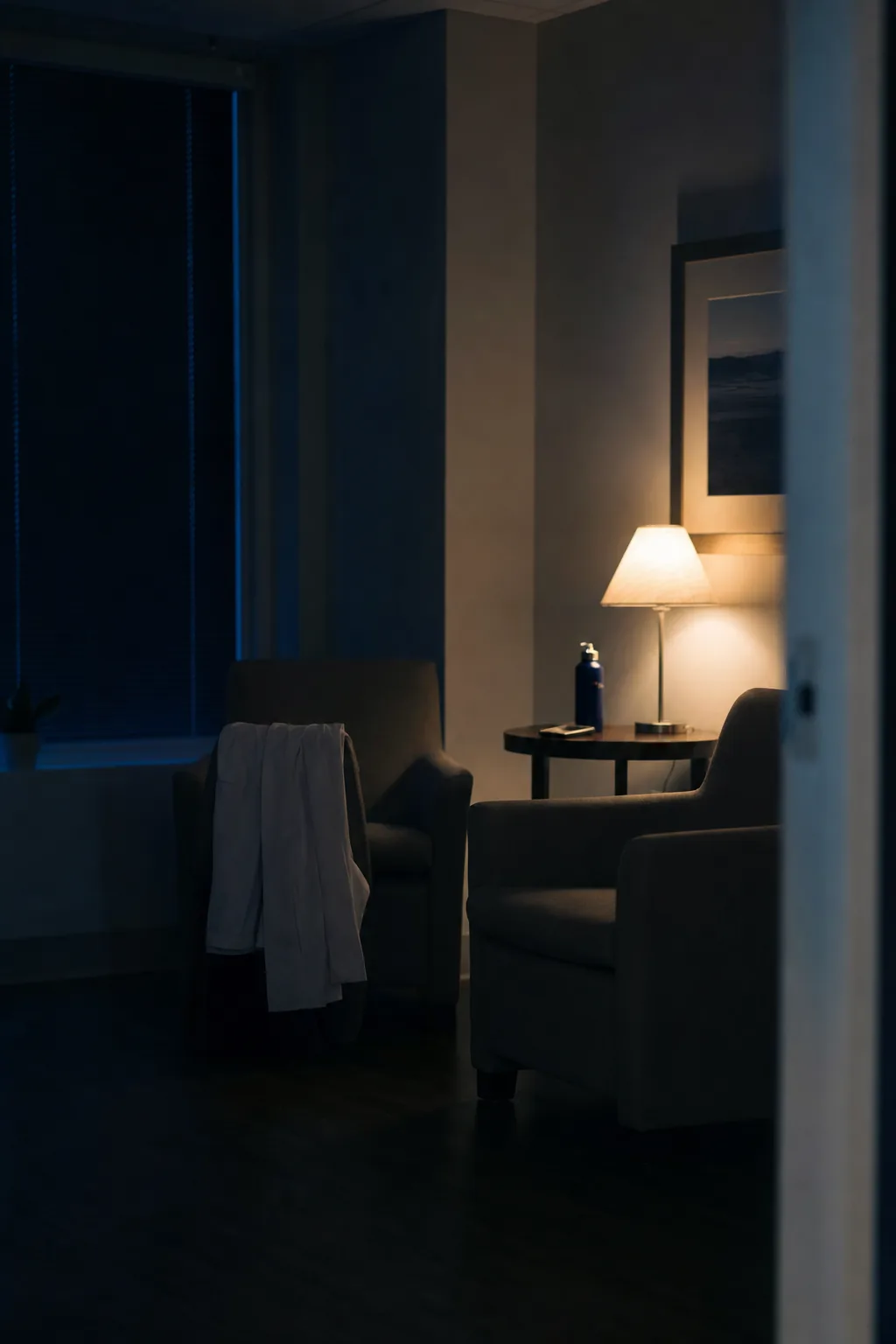 An empty physicians' lounge at night, one lamp lit, a coat left over a chair.